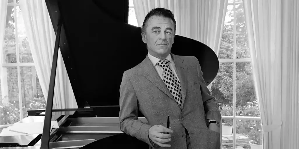 A man in suit and tie standing next to piano.