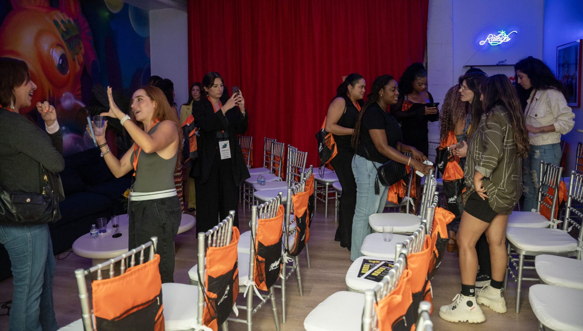 A group of people standing around chairs in front of tables.