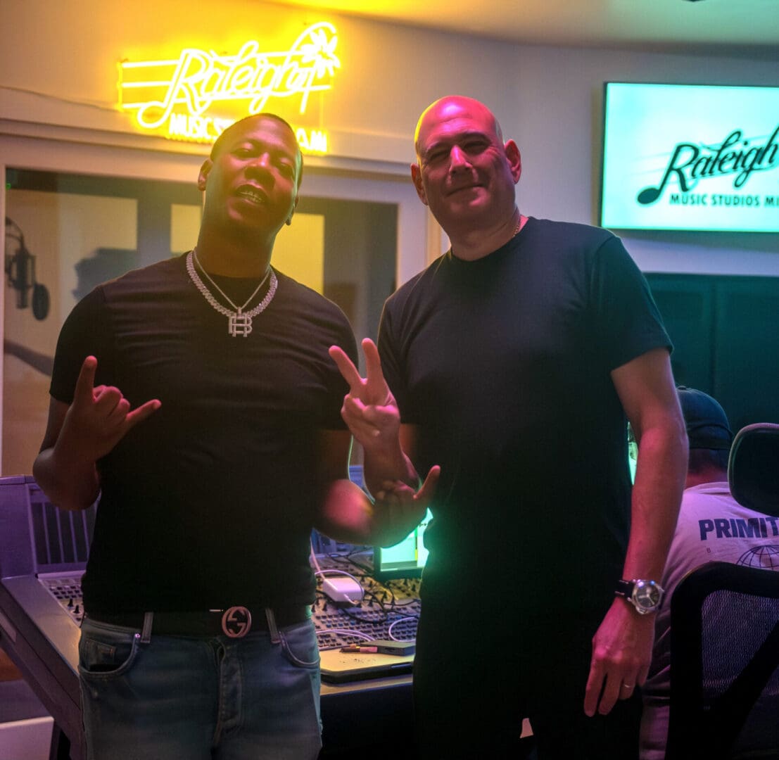 Two men pose for a picture in front of neon lights.