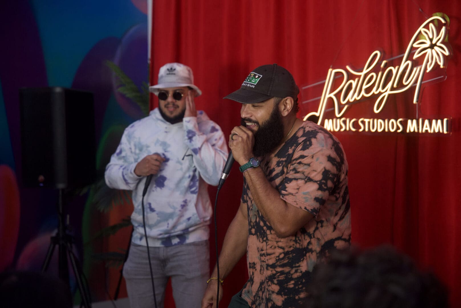 Two men are singing in front of a red curtain.