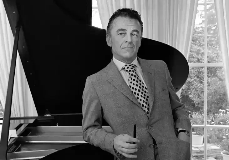 A man in suit and tie standing next to piano.